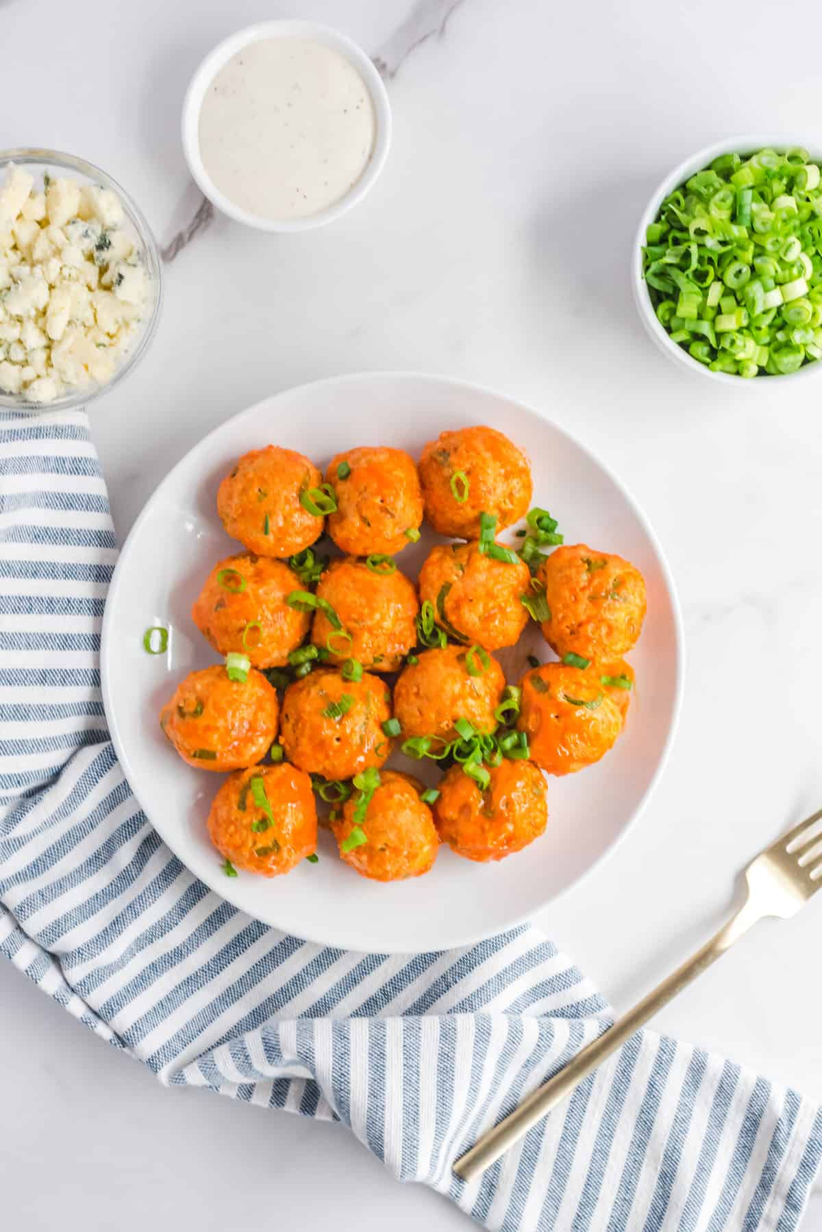 Chicken meatballs arranged on a white plate topped with diced green onions.