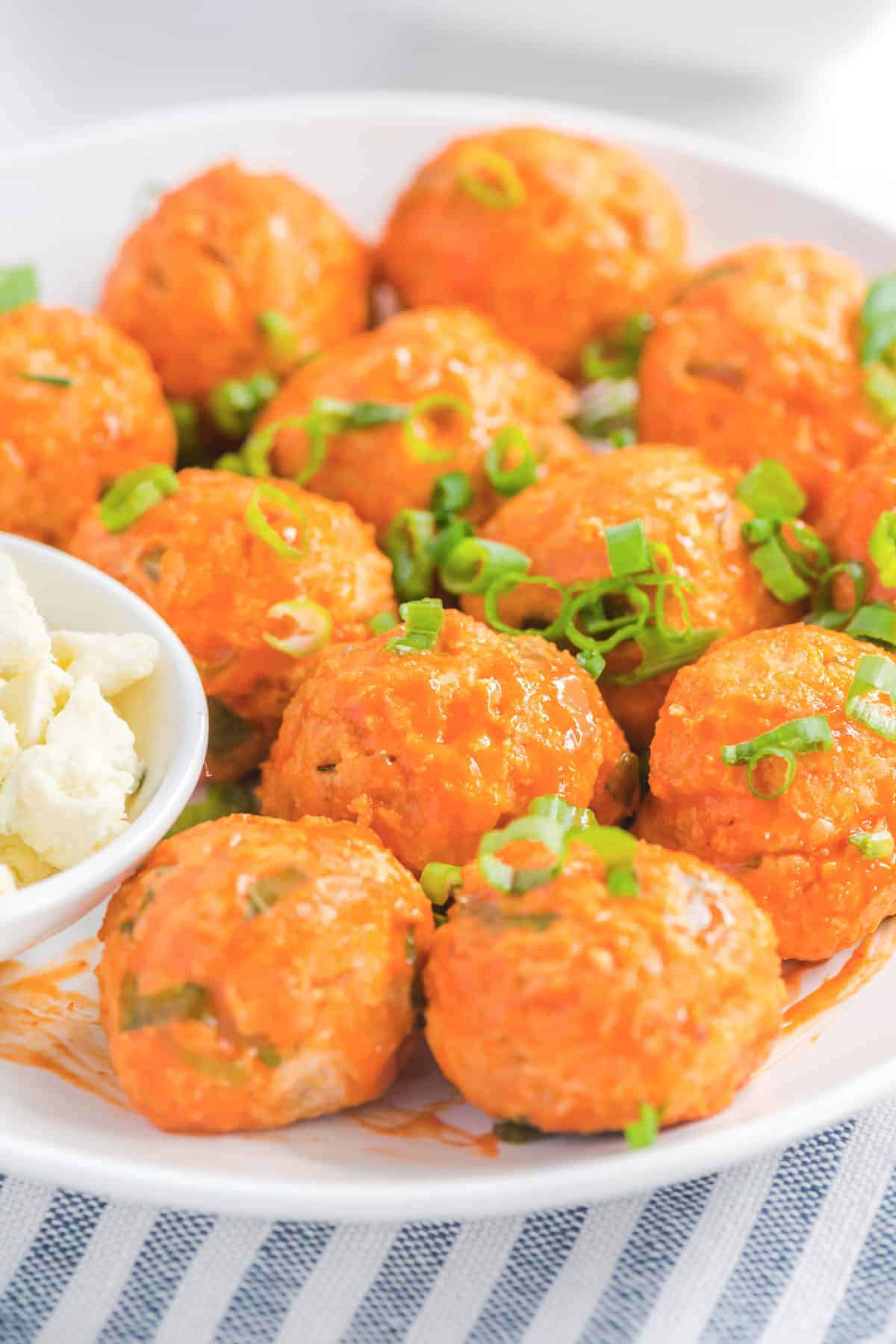 Close up photo of chicken meatballs arranged on a white plate topped with diced green onions.