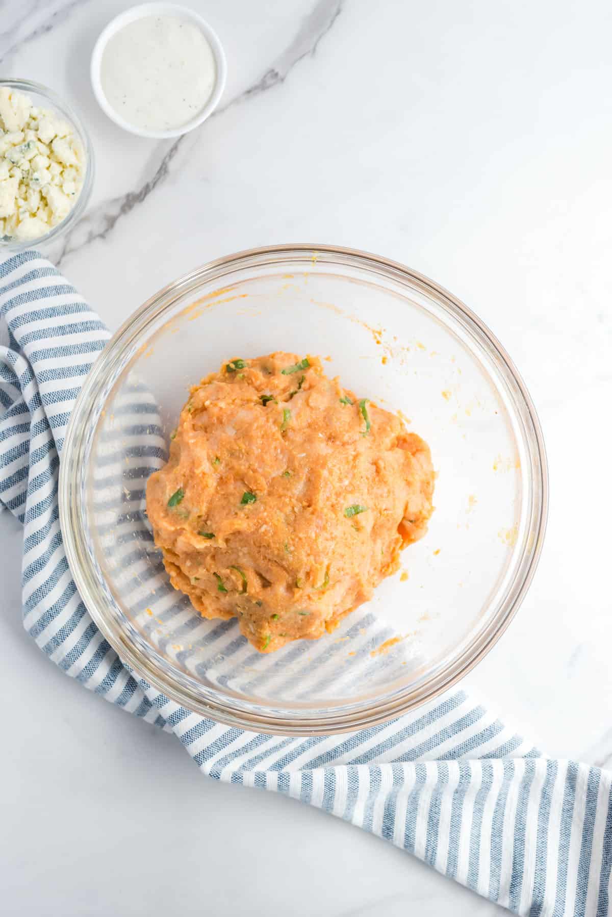All ingredients for chicken meatballs mixed together in a glass mixing bowl.