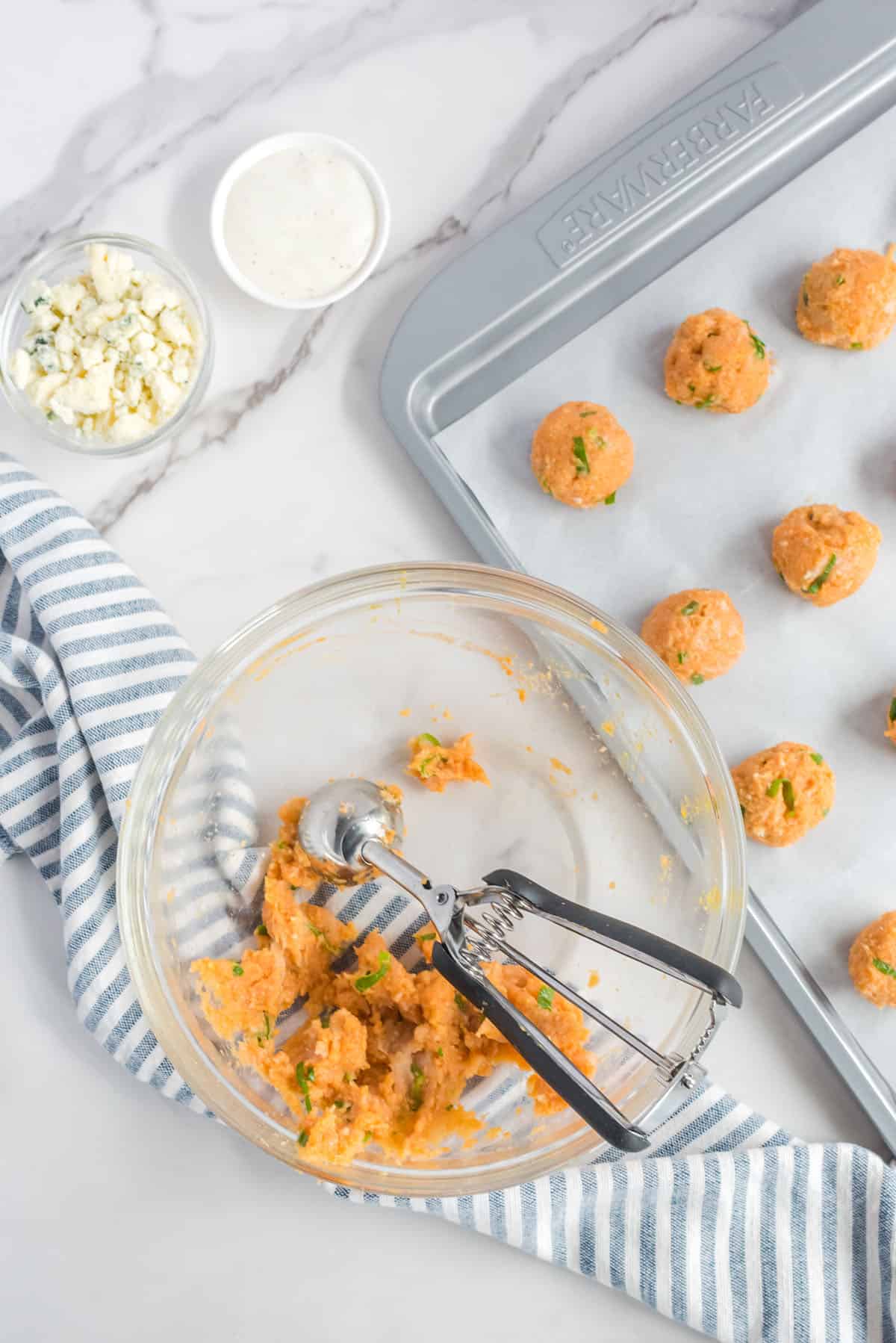 All ingredients for chicken meatballs being scooped with a cookie scoop onto parchment paper-lined baking sheet.