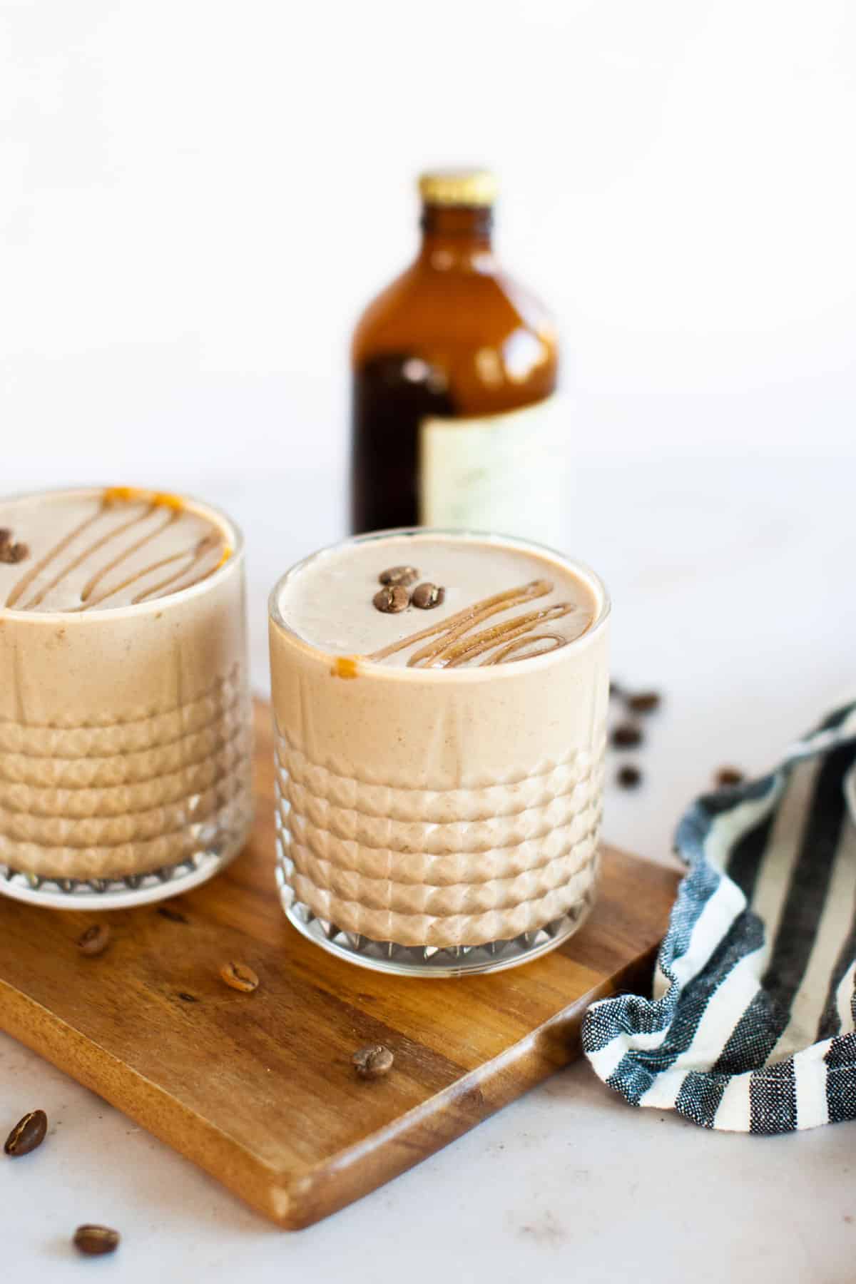 Coffee smoothies sitting on a cutting board with an amber bottle of cold brew in the background.