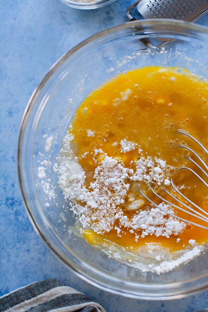 Egg, sugar and flour being mixed in glass mixing bowl.