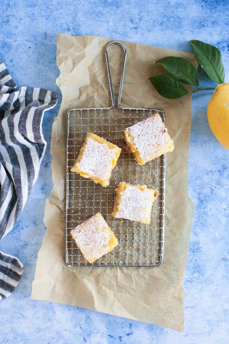 Lemon bar squares with powdered sugar arranged on a rectangular wire rack.