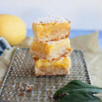 Three lemon bar slices stacked on top of a wire cooling rack.