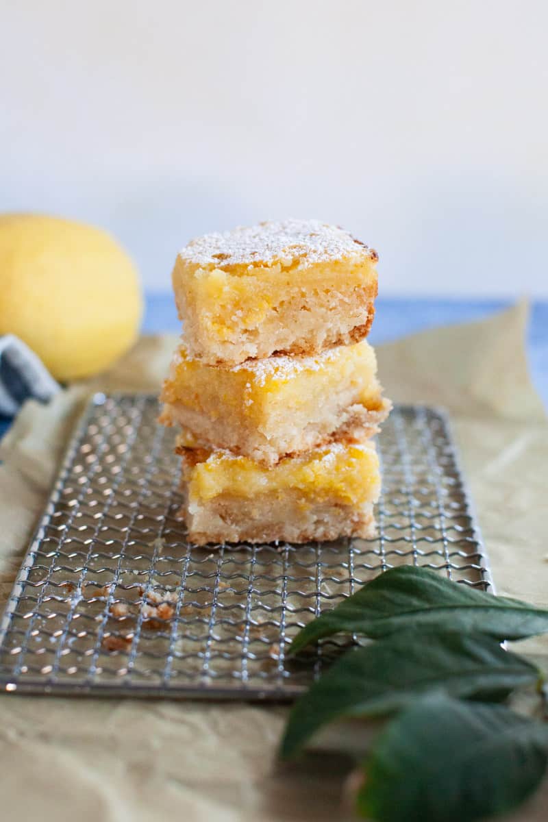 Three lemon bar slices stacked on top of a wire cooling rack.