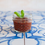 a small jar of pizza sauce with basil leaves on blue tiles.