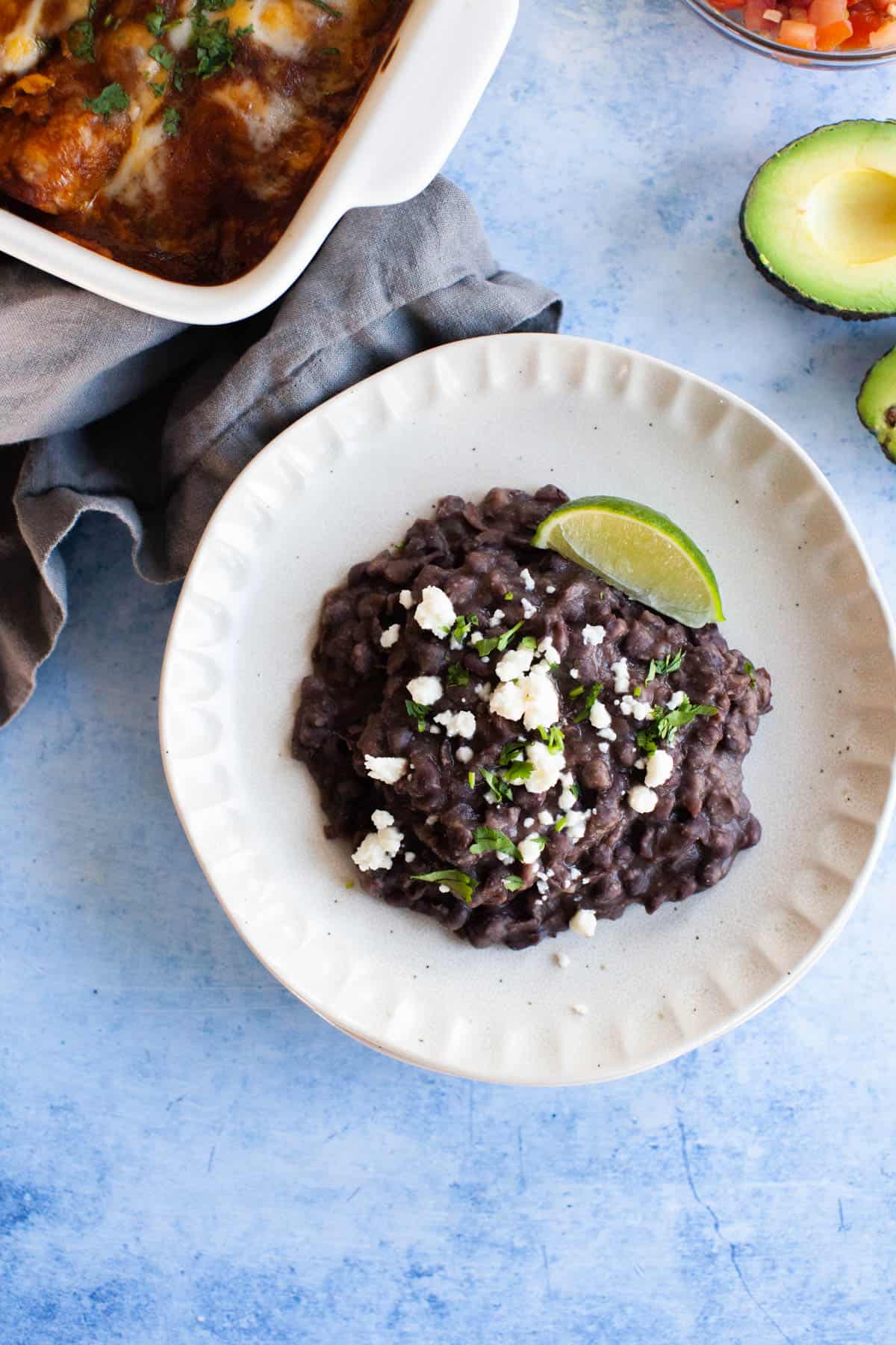 Overhead refried black beans topped with cotija cheese and a lime wedge situated on a small white plate.