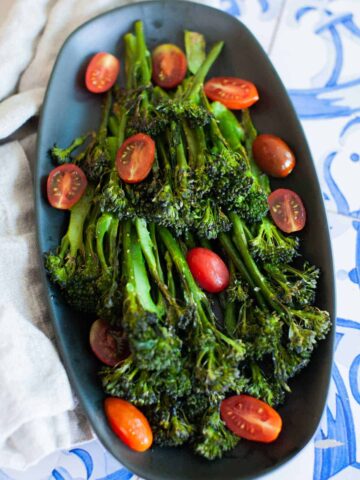 An overhead shot of roasted broccolini garnished with sliced cherry tomatoes.