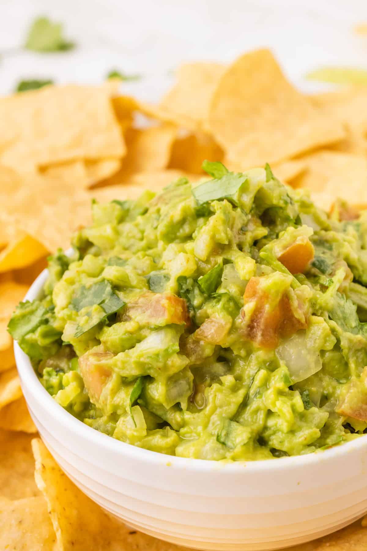 Easy guacamole in a white serving bowl on a bed of tortilla chips.