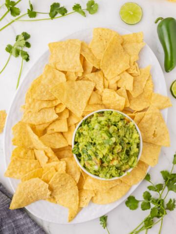 Easy guacamole in a white serving bowl on a plate of tortilla chips.