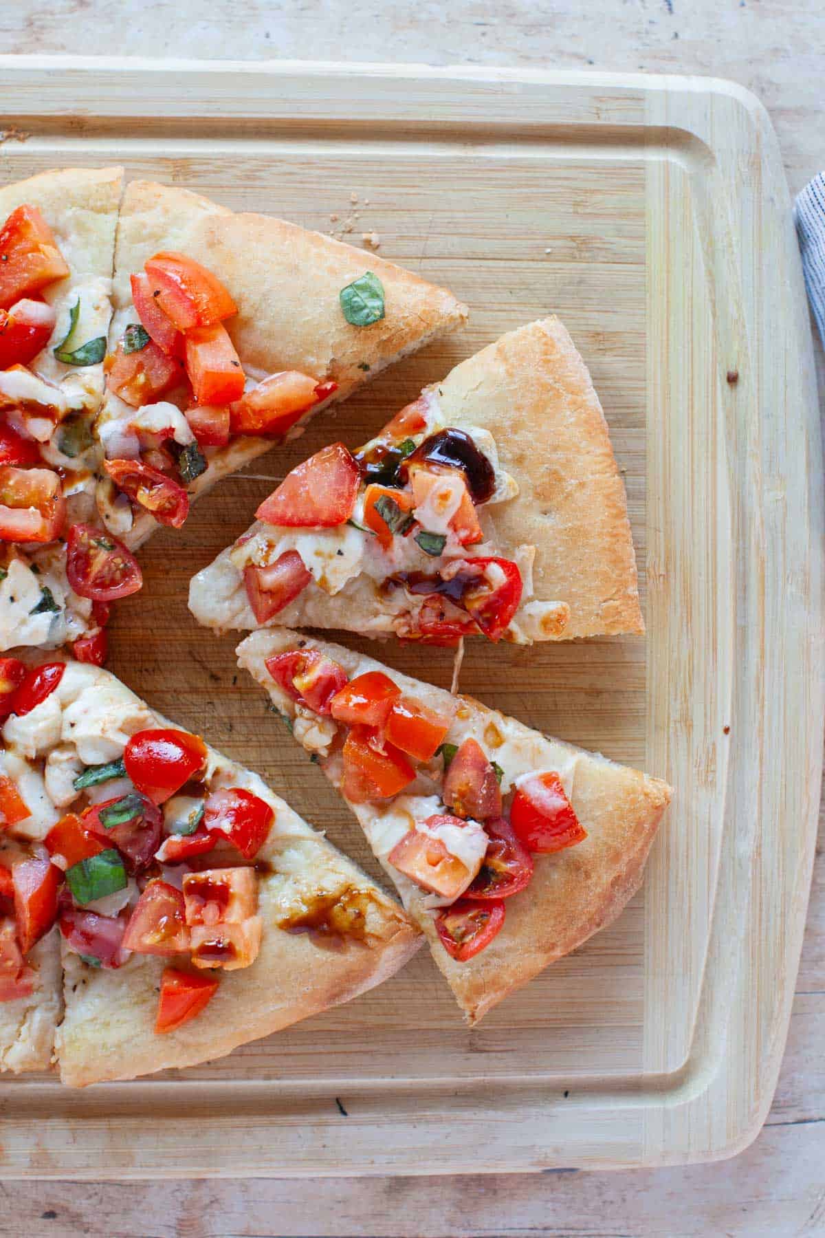 Sliced bruschetta pizza on a wooden cutting board.