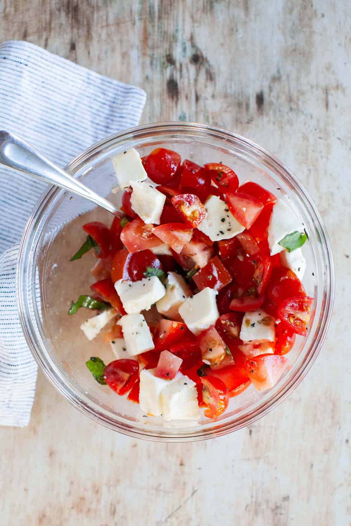 Bruschetta mixture in a glass bowl, sitting on a bamboo cutting board.