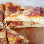 One slice of grilled pizza being pulled from the pie with a small cheese pull from the rest of the pie.