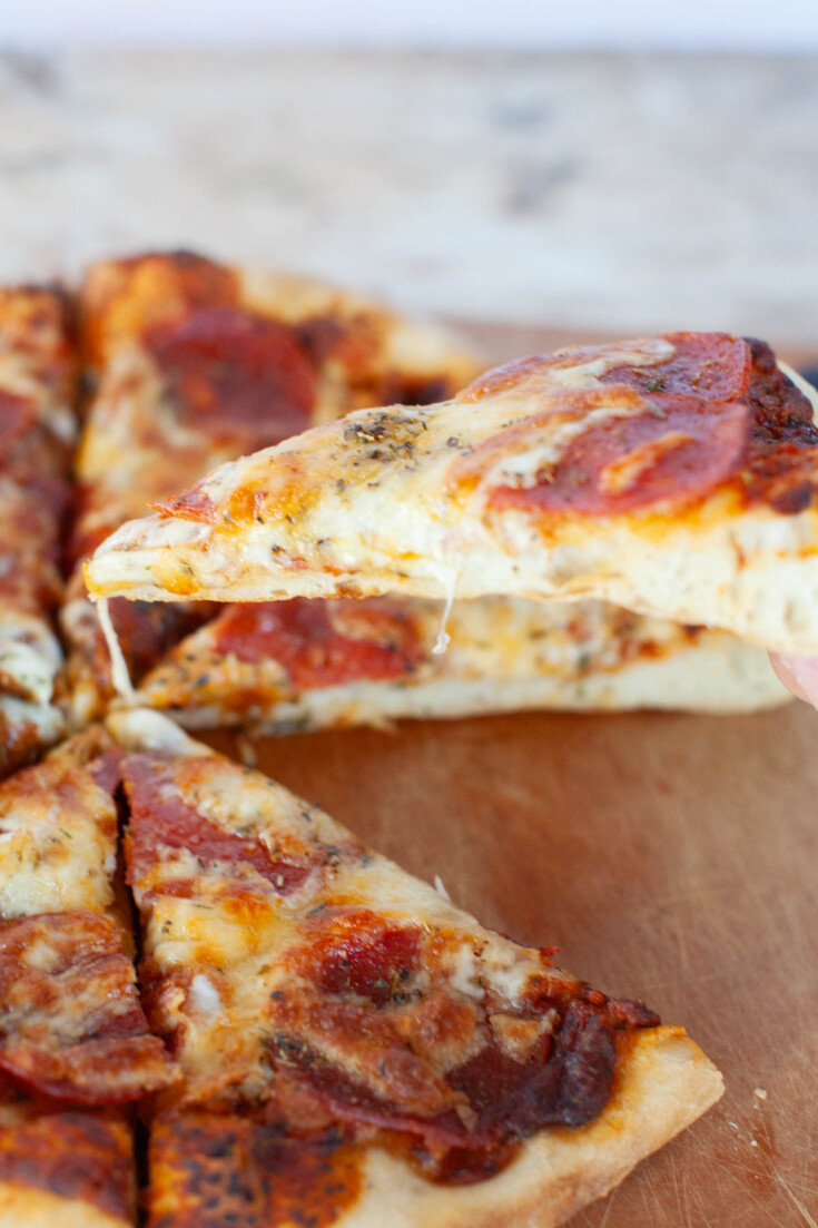 One slice of grilled pizza being pulled from the pie with a small cheese pull from the rest of the pie.
