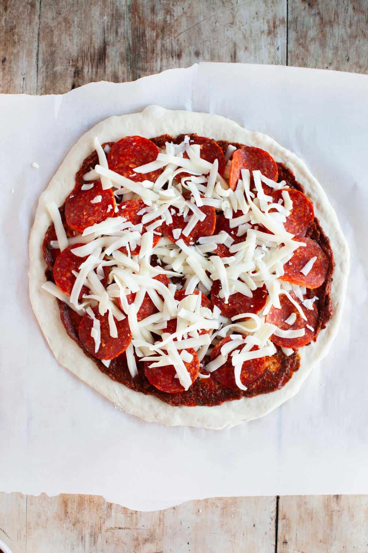 Sliced pepperoni on top of pizza dough with pizza sauce and shredded mozzarella.