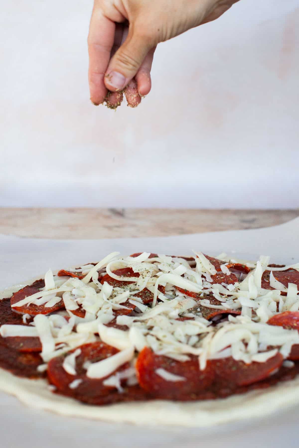 Fully prepped grilled pizza being hand sprinkled with pizza seasoning.