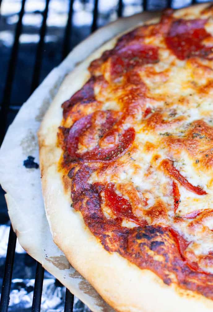 smoked pizza with pepperoni and cheese on a grill.