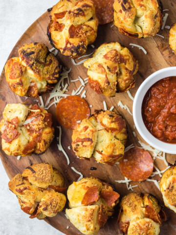 Pizza muffins arranged on a circular, wooden serving dish with marinara sauce on the side.