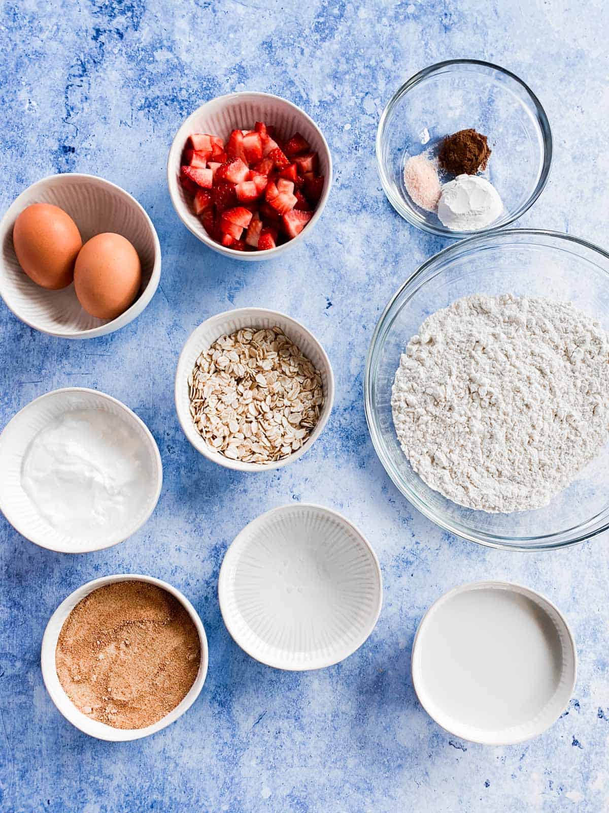 Wet strawberry muffin ingredients in separate glass and porcelain bowls.