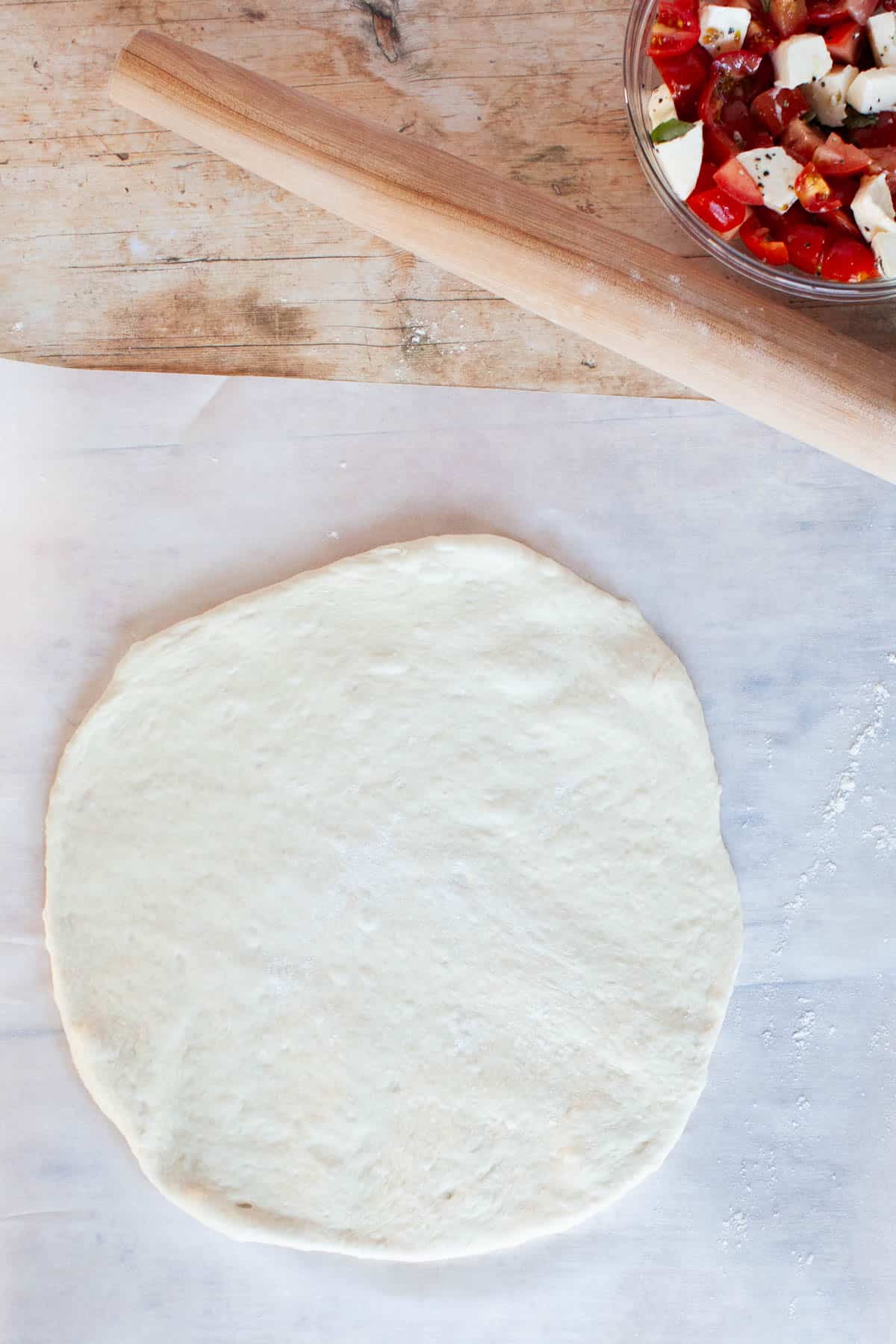 Thin crust pizza dough flatly rolled out on parchment paper.