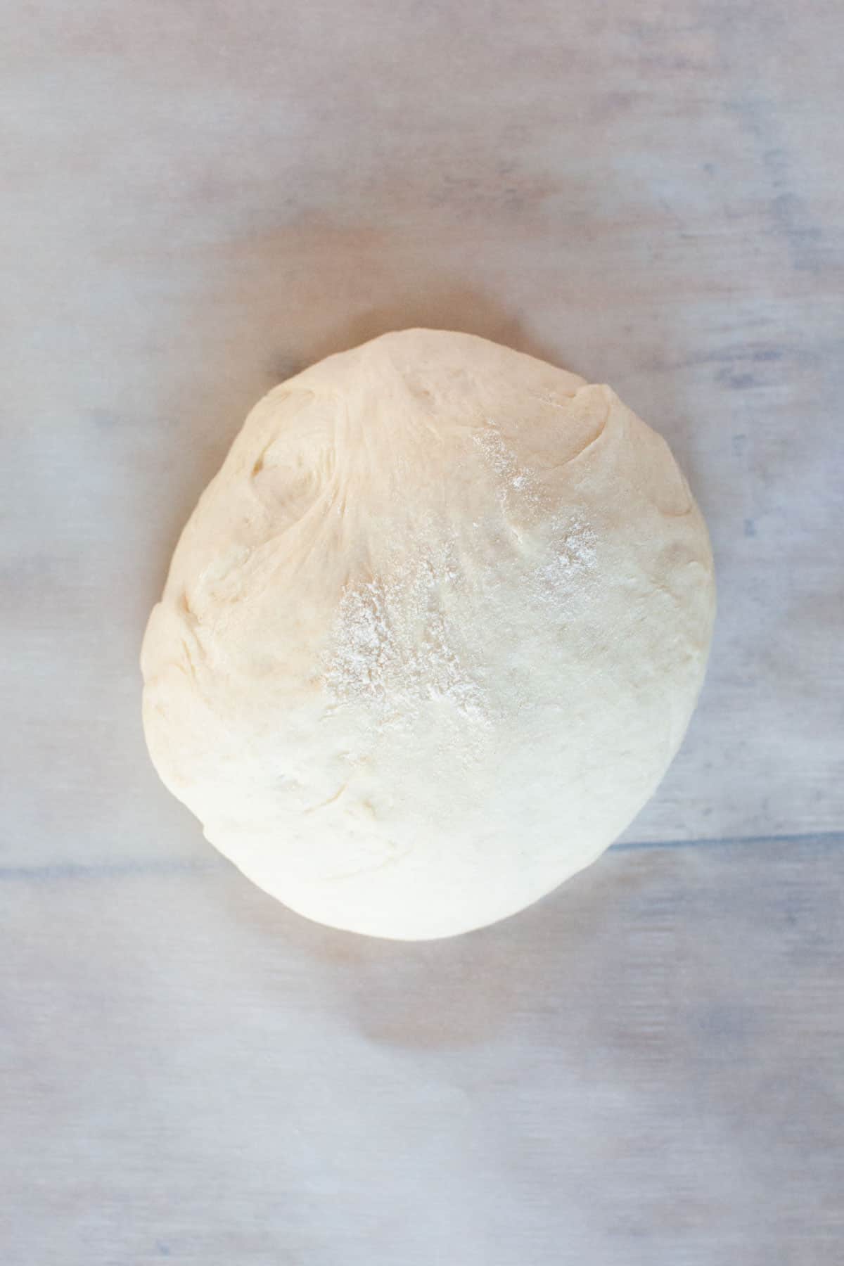 Thin crust pizza dough on parchment paper on wooden countertop.