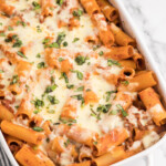 Baked rigatoni with melted, shredded cheese in a white serving dish.