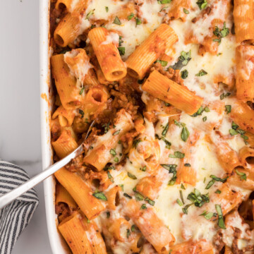 Overhead photo of baked rigatoni with melted, shredded cheese in a white serving dish.