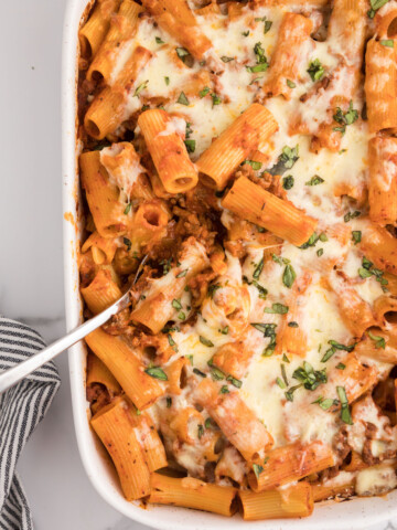 Overhead photo of baked rigatoni with melted, shredded cheese in a white serving dish.