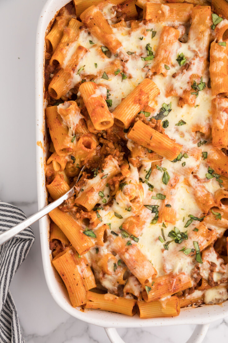 Overhead photo of baked rigatoni with melted, shredded cheese in a white serving dish.