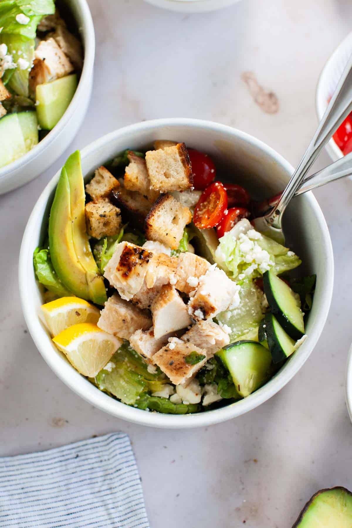 Grilled chicken salad served in a white bowl with forks.