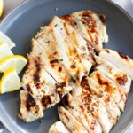 Thinly, sliced grilled chicken breasts with lemon wedges on a small, gray plate.
