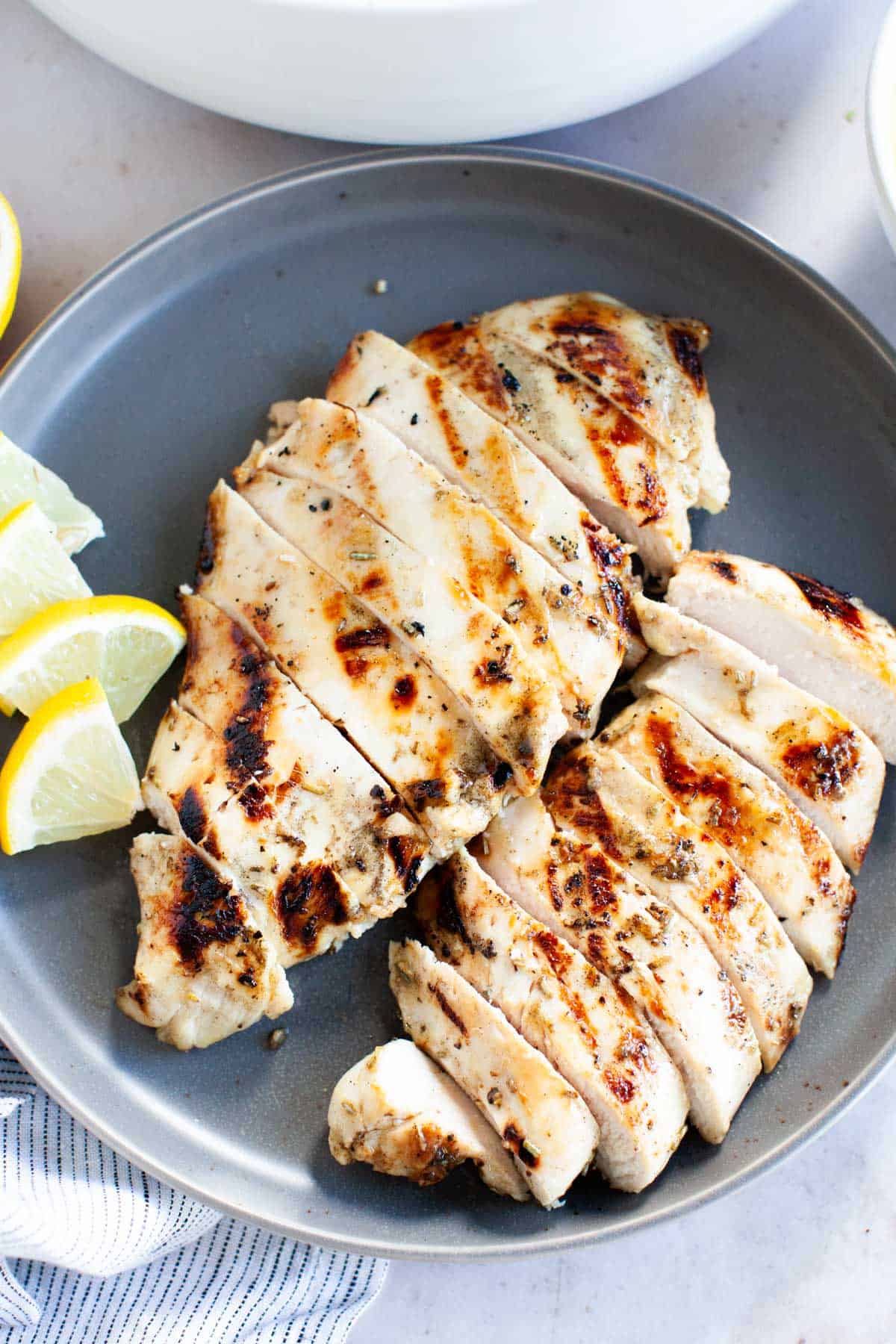 Thinly, sliced grilled chicken breasts with lemon wedges on a small, gray plate.