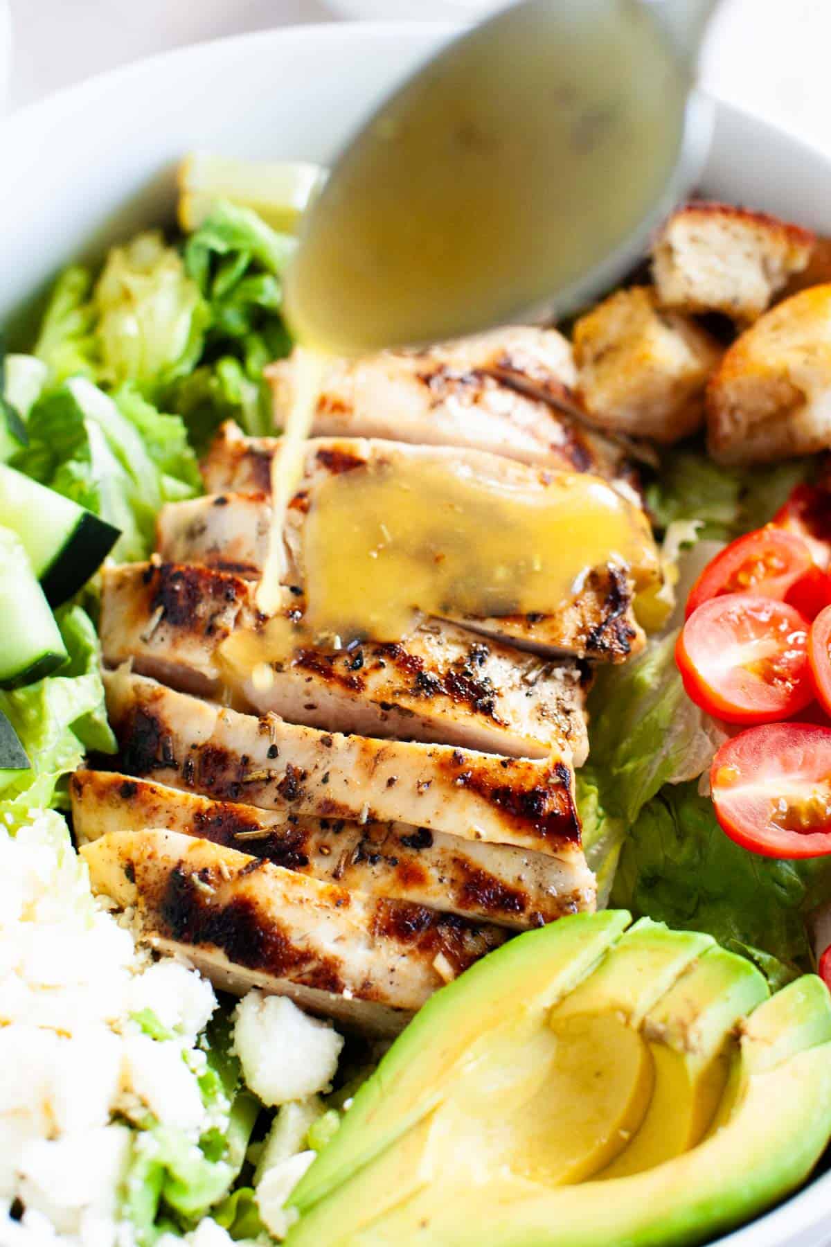 A honey vinaigrette dressing being drizzled onto the grilled chicken salad.