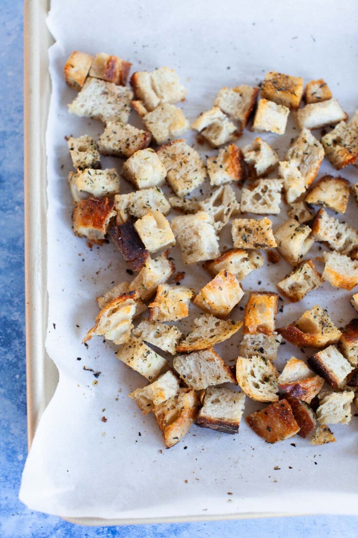 Fully baked homemade croutons on the parchment-paper lined baking sheet.