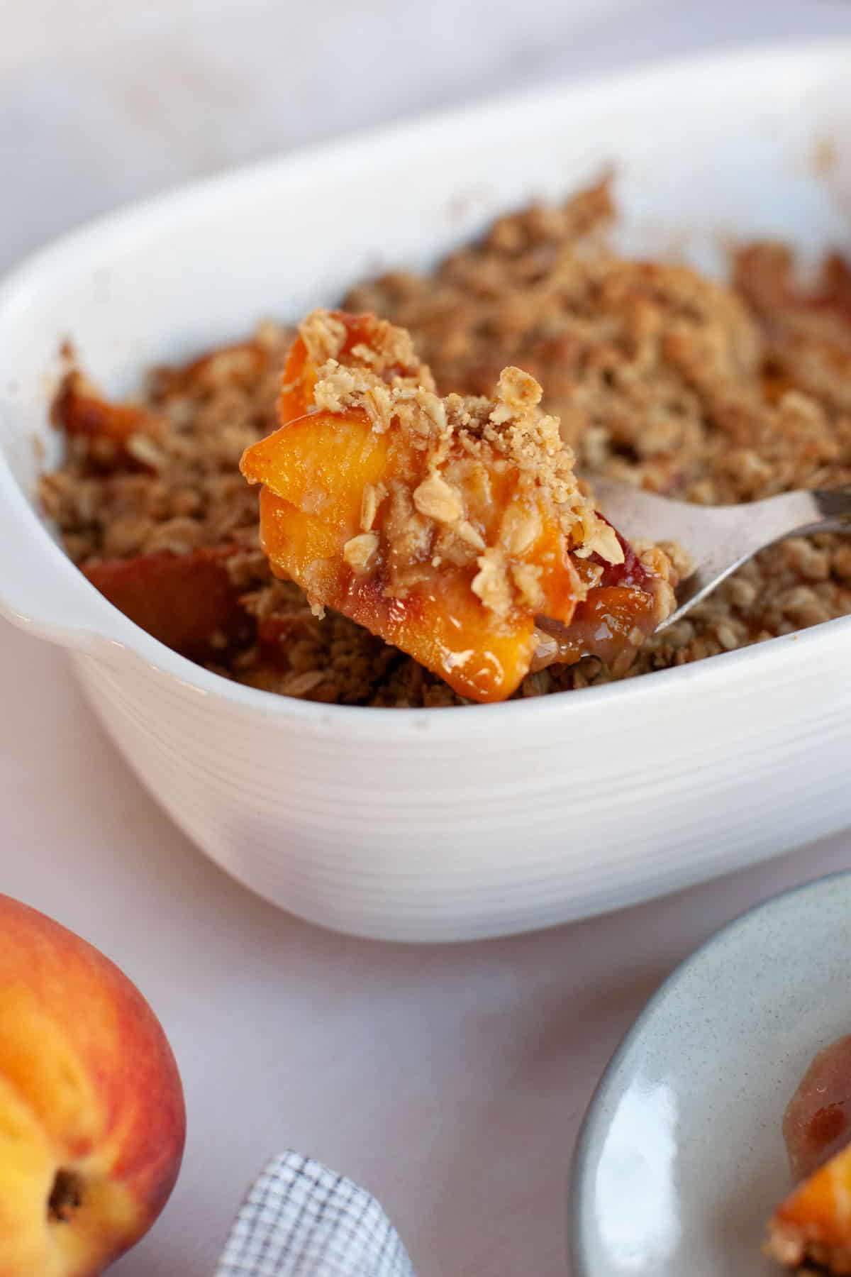A small serving of peach crisp being spooned out of a white serving dish.