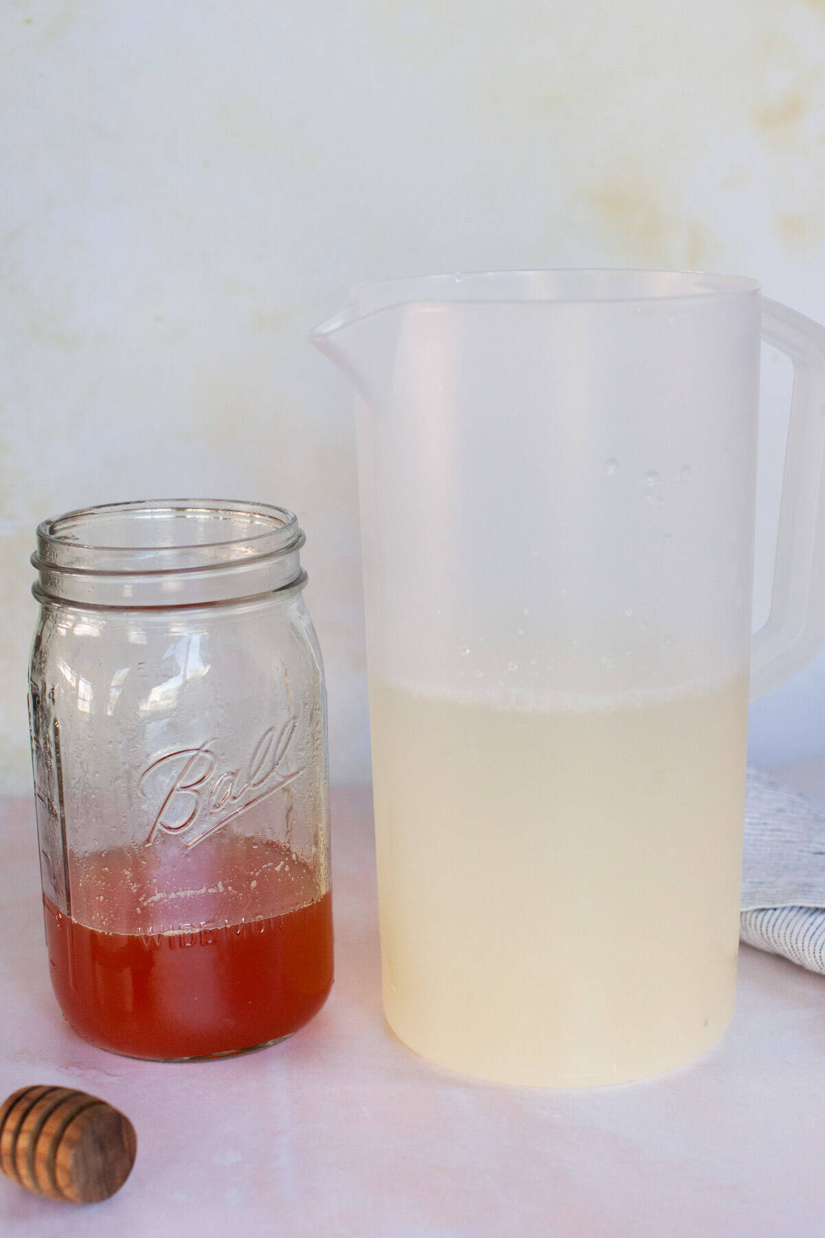 Lemonade in a pitcher, sitting next to a jar of peach simple syrup.