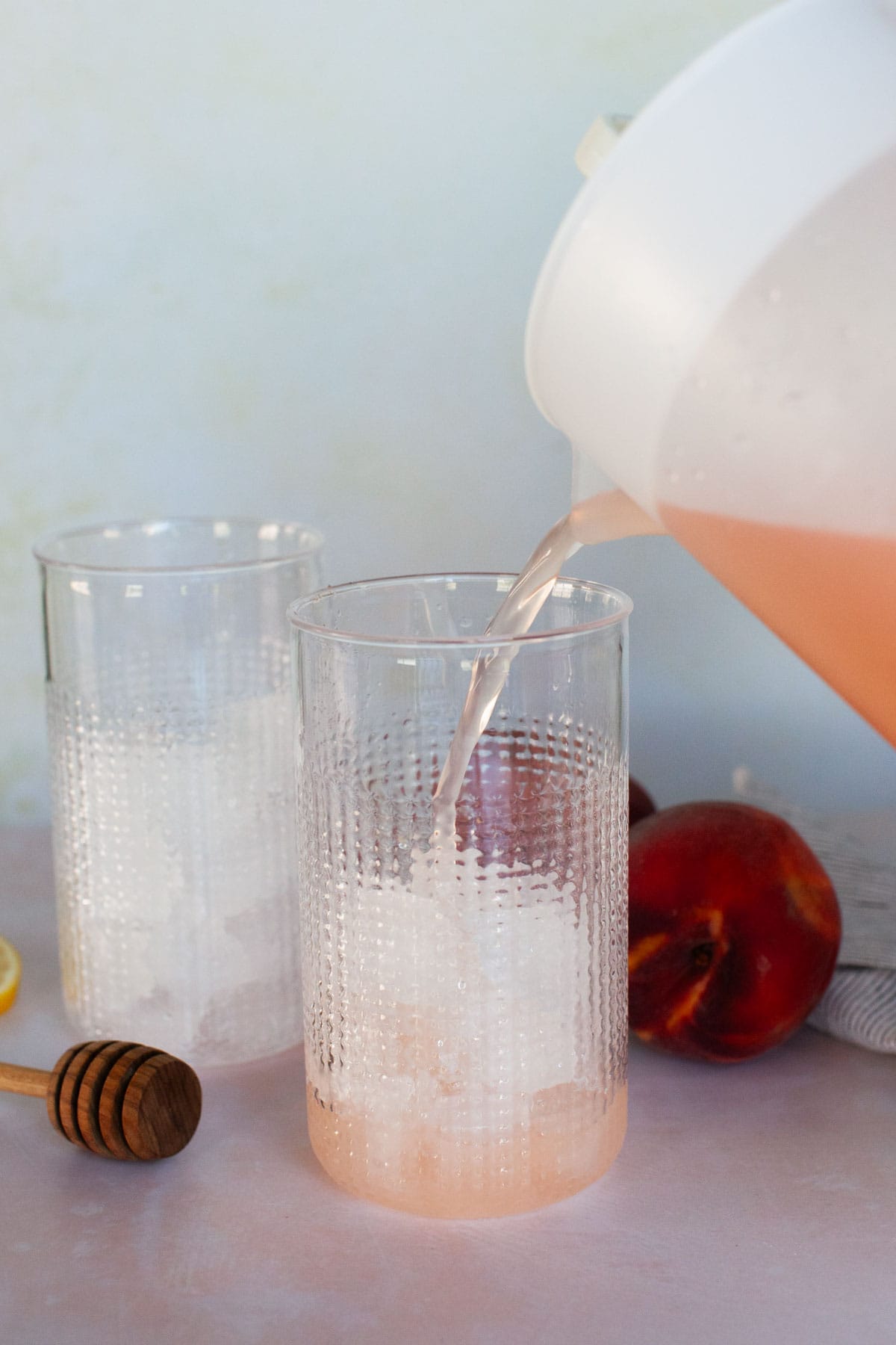 Peach lemonade being poured into glasses full of ice.