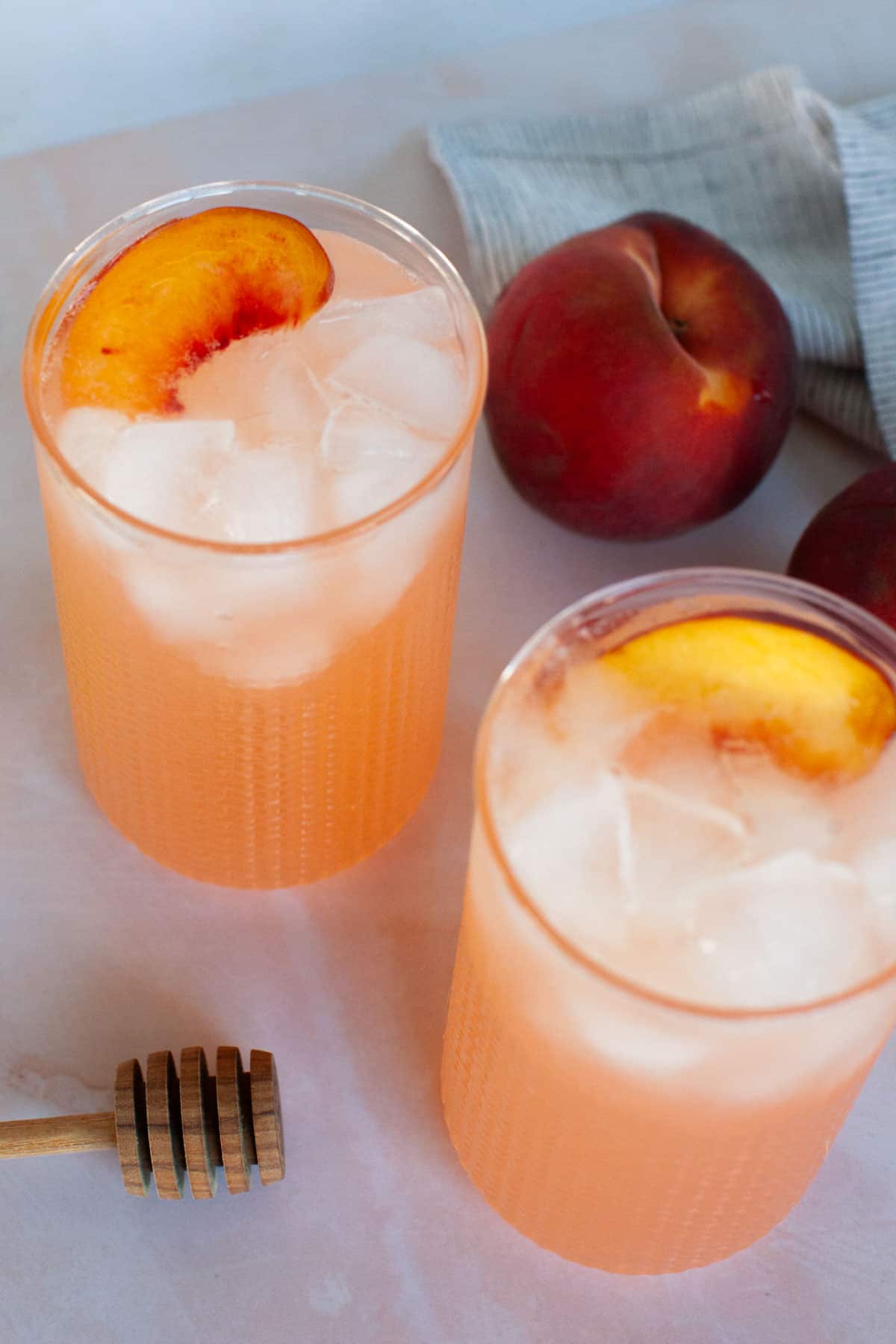 An overhead shot of two glasses of peach lemonade, garnished with peach slices.