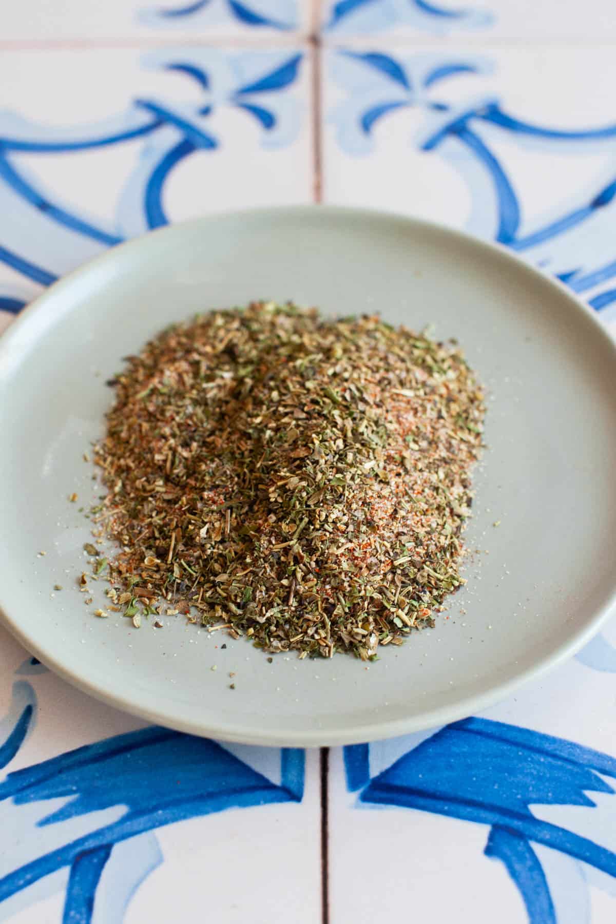 Close up photo of pizza seasoning arranged a small plate on a blue and white tile counter.