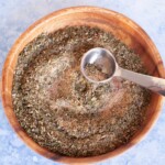 A wooden bowl filled with pizza seasoning herbs and spices.