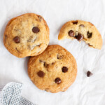Two walnut chocolate chip cookies next to a half cookie on a sheet of parchment paper.