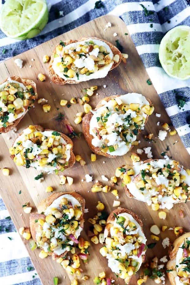 Corn on the cob on a cutting board with lime wedges.