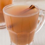 A clear mug of spiced apple cider with a whole cinnamon stick.
