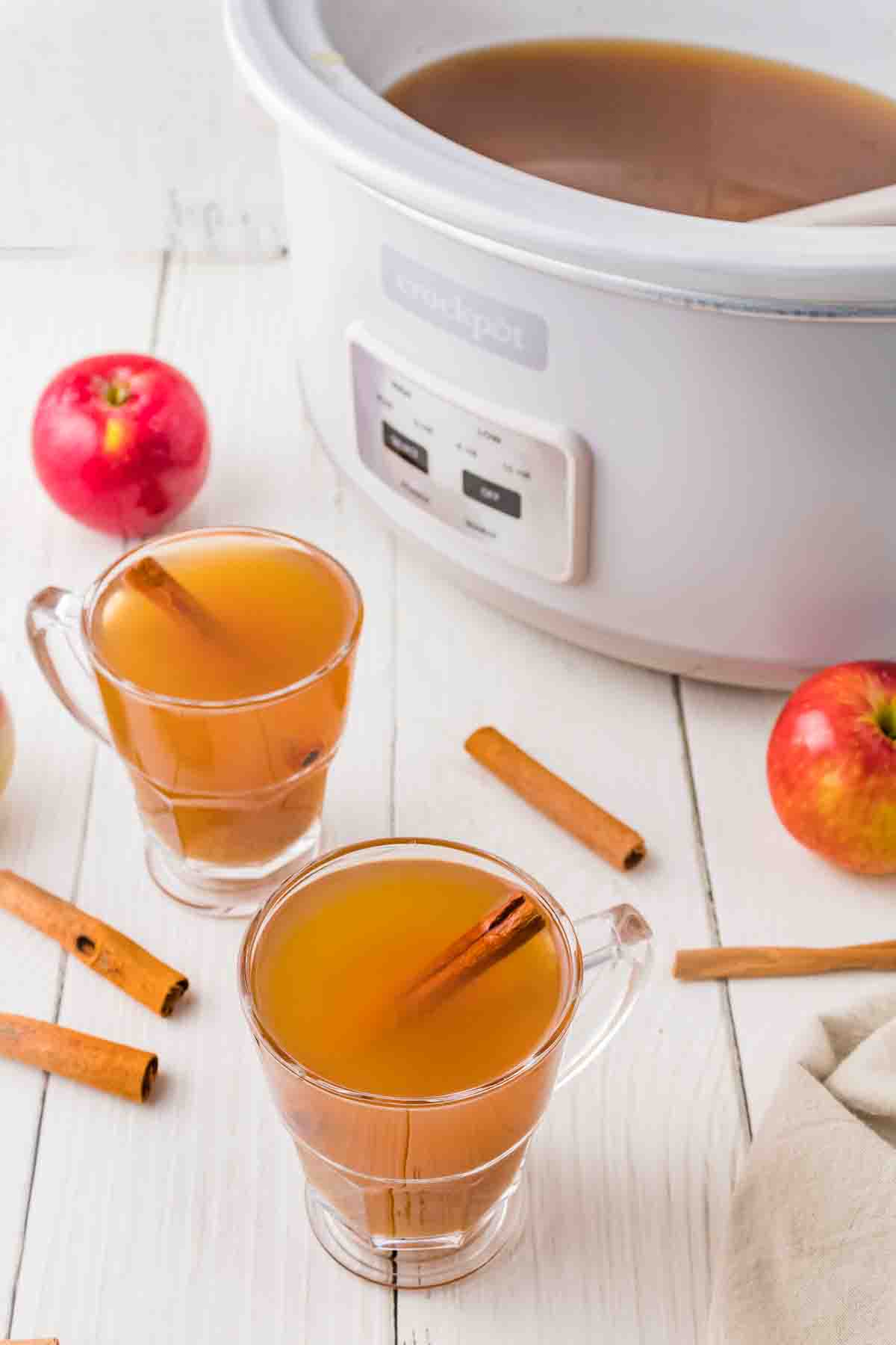 Two glass mugs of apple cider in front of a crockpot.