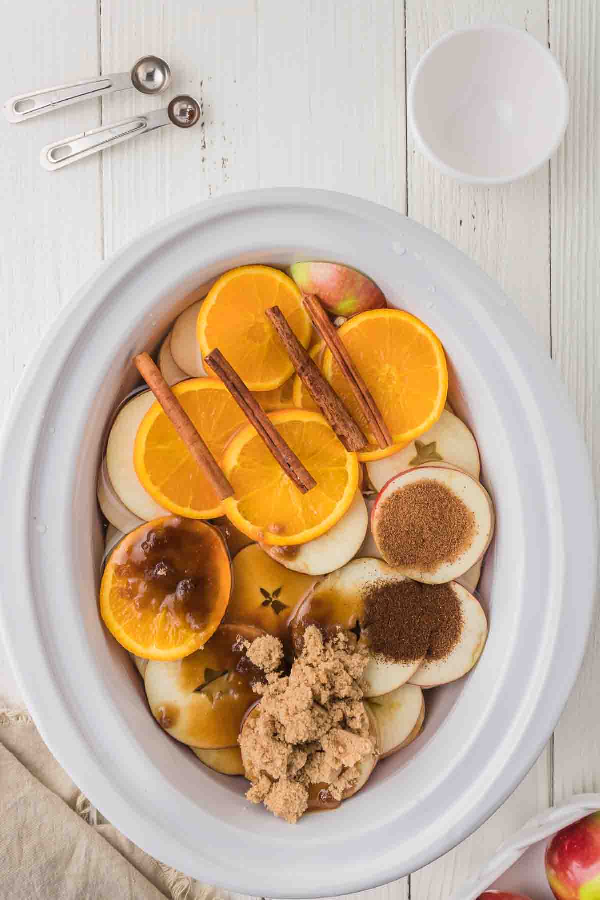 Sliced apples and oranges topped with cinnamon sticks, brown sugar, and vanilla.