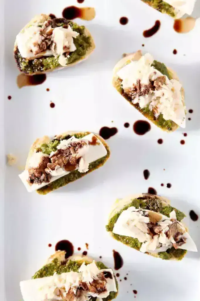 Crostini with pesto and cheese on a white plate.