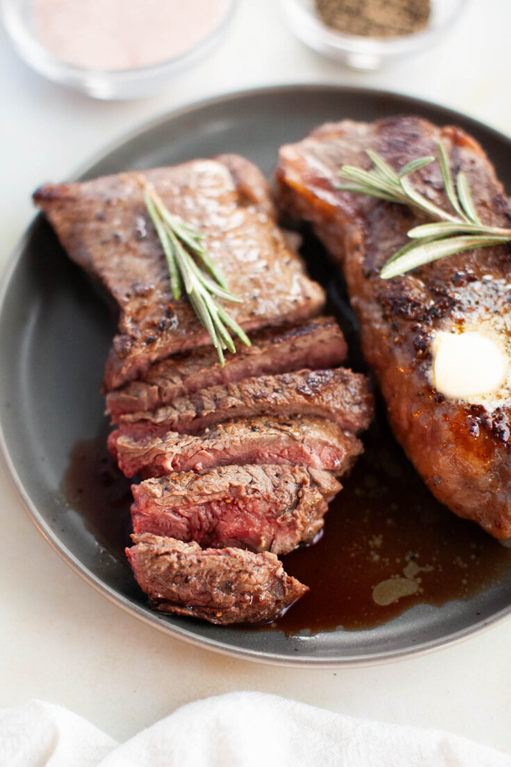 Sliced steak on a plate with rosemary sprigs and melted butter.