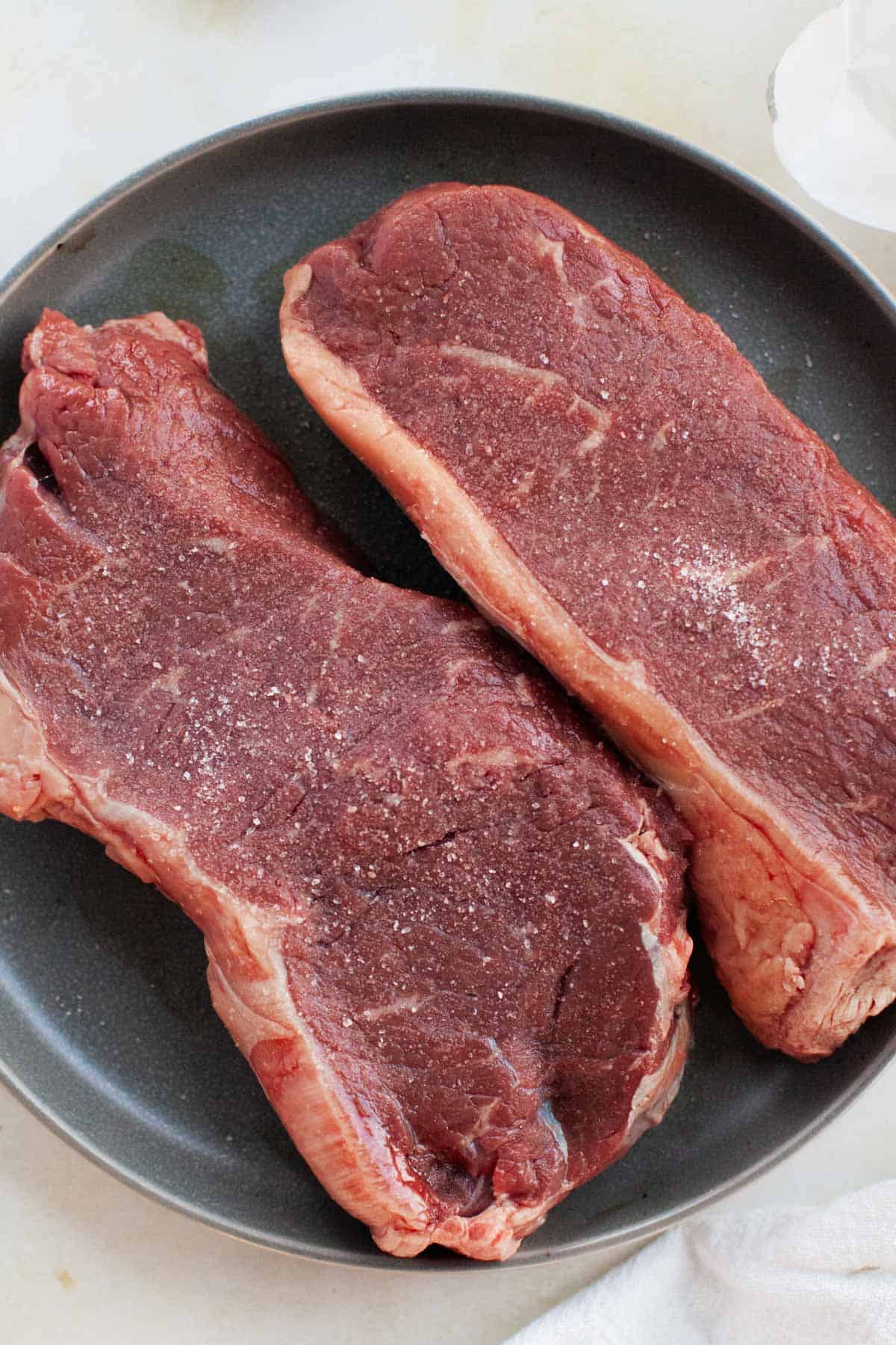 Two steaks on a plate sprinkled with salt.