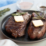 Two steaks on a plate with butter and rosemary.