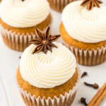 Pumpkin cupcakes topped with cream cheese icing and star anise on a white serving tray.